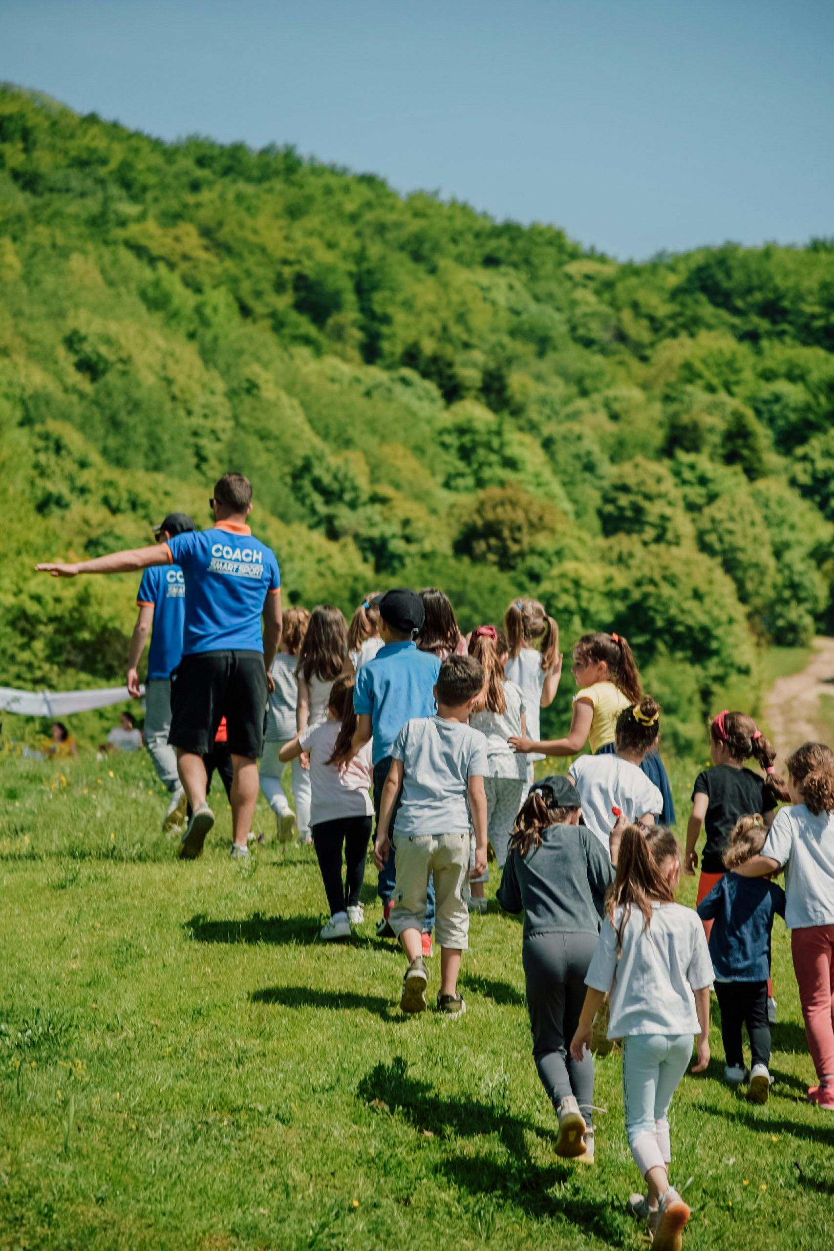 A group of children with coaches walking outdoors in a lush green area during a school trip.